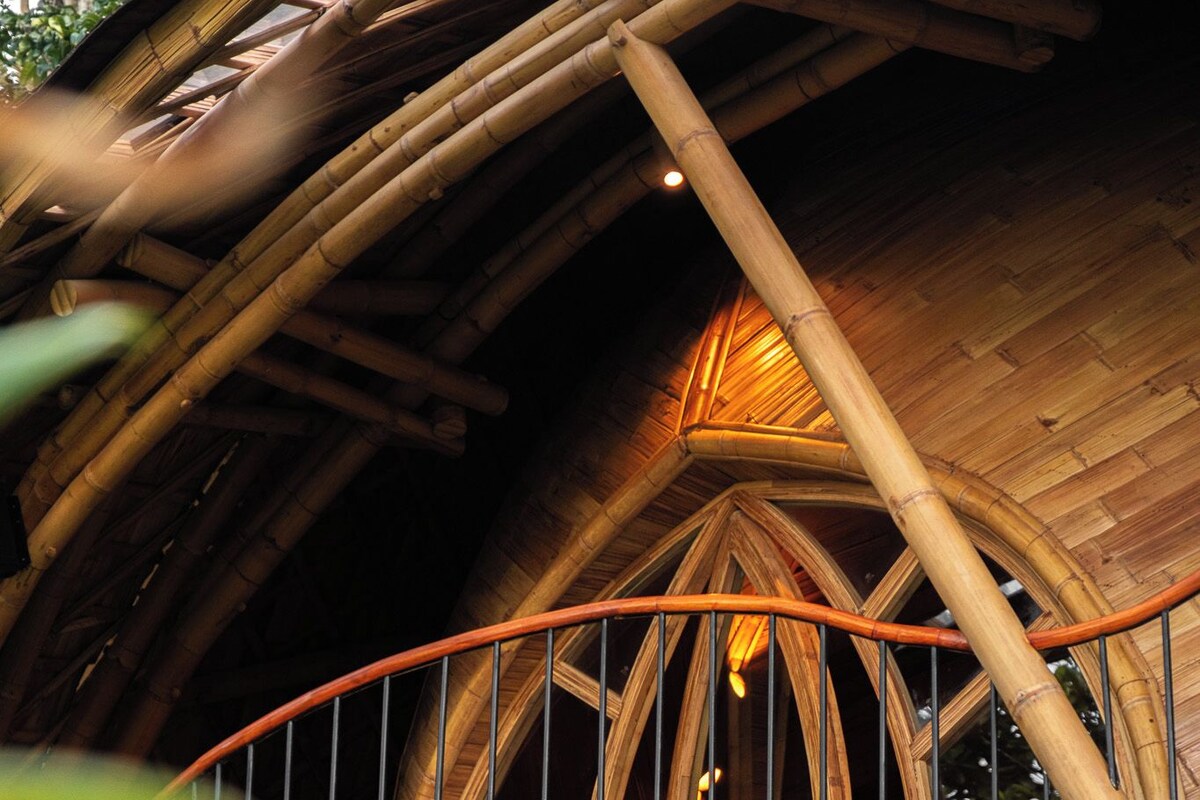A bamboo structure with a curved balcony and large green leaves in the foreground.