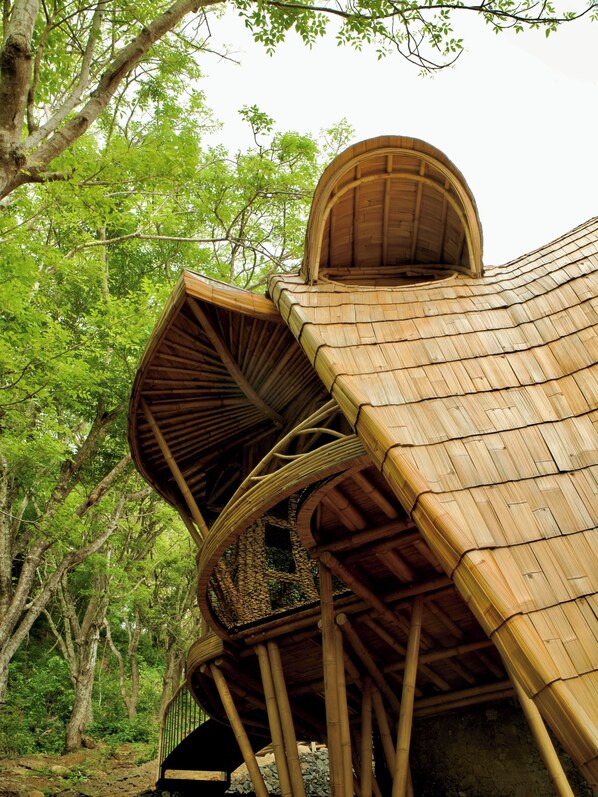 A bamboo structure with a curved roof, surrounded by trees. - Cocoon Reserve (Kuta)