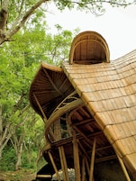 A bamboo structure with a curved roof, surrounded by trees.