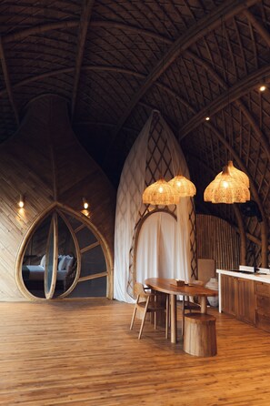 A room with a high, curved ceiling, a round mirror, a dining table, and two hanging lamps. - Cocoon Reserve (Kuta)