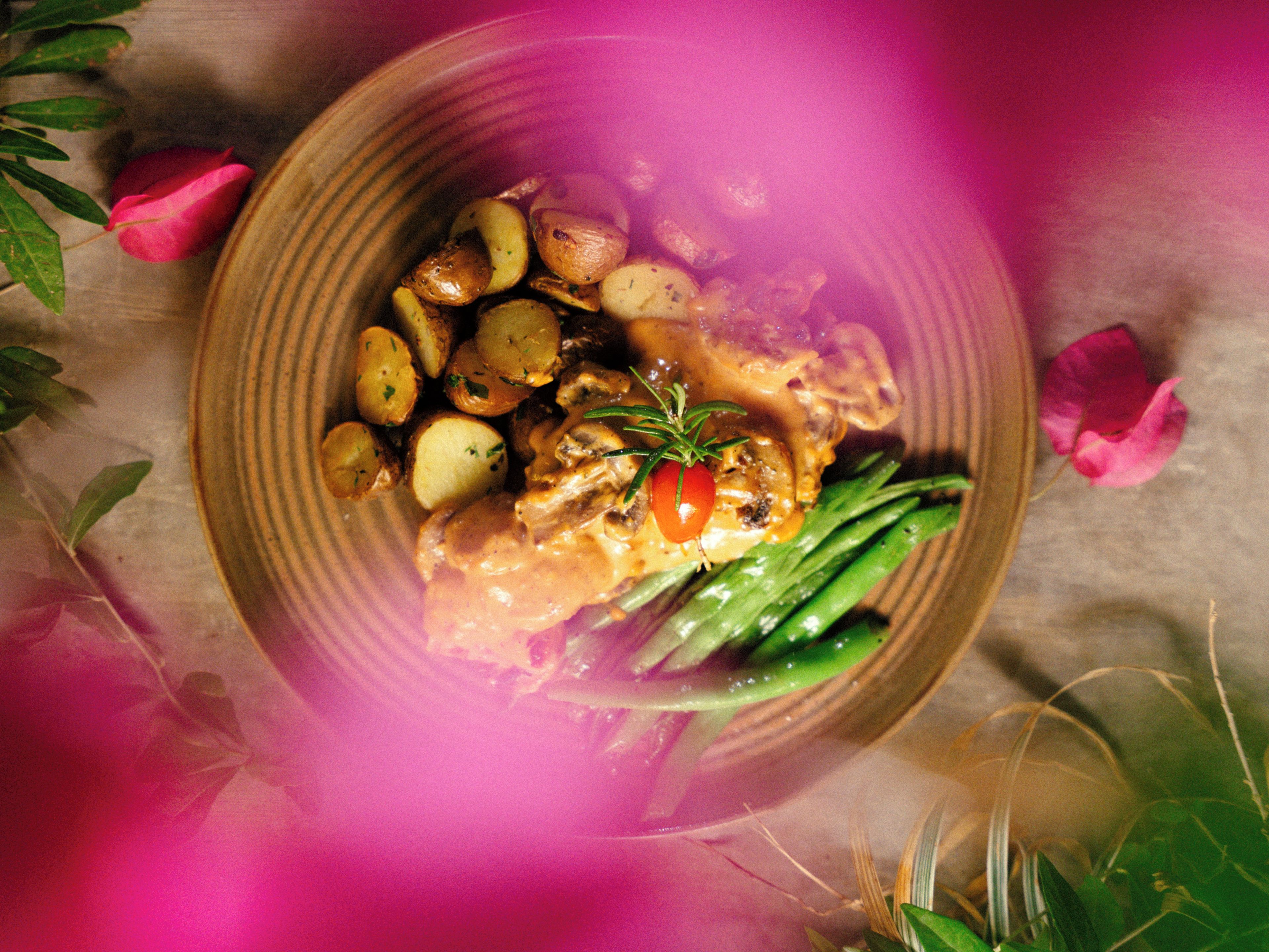 A plate of food with potatoes, mushrooms, and green beans, garnished with a cherry tomato and a sprig of rosemary.