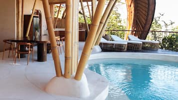 Un espace piscine agrémenté de piliers en bambou, de chaises longues et d’une table à manger.