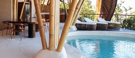 A pool area with bamboo pillars, lounge chairs, and a dining table.