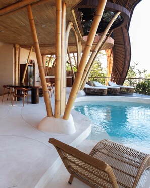 A pool area with bamboo pillars, lounge chairs, and a dining table. - Cocoon Reserve (Kuta)