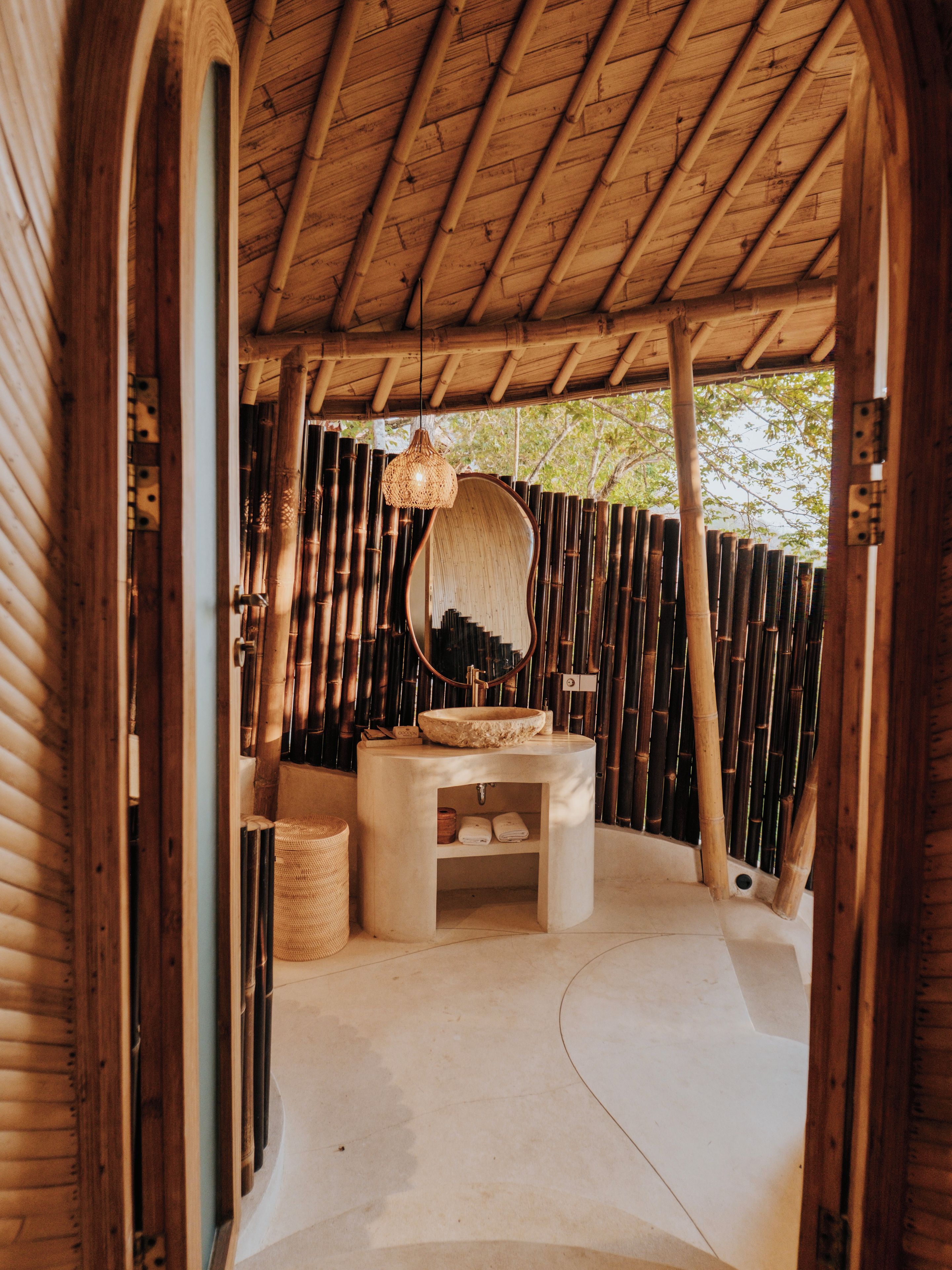 Interior de madera con un lavabo circular, una lámpara colgante y una pared de bambú.