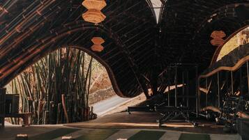 Un espacio interior con una estructura de techo curva, equipo de ejercicio y colchonetas en el suelo.