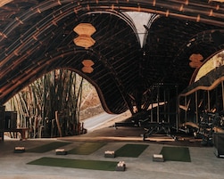 An indoor space with a curved ceiling structure, exercise equipment, and mats on the floor.