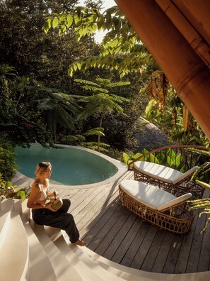 Une personne assise au bord d’une piscine, avec des chaises longues et une terrasse en bois.