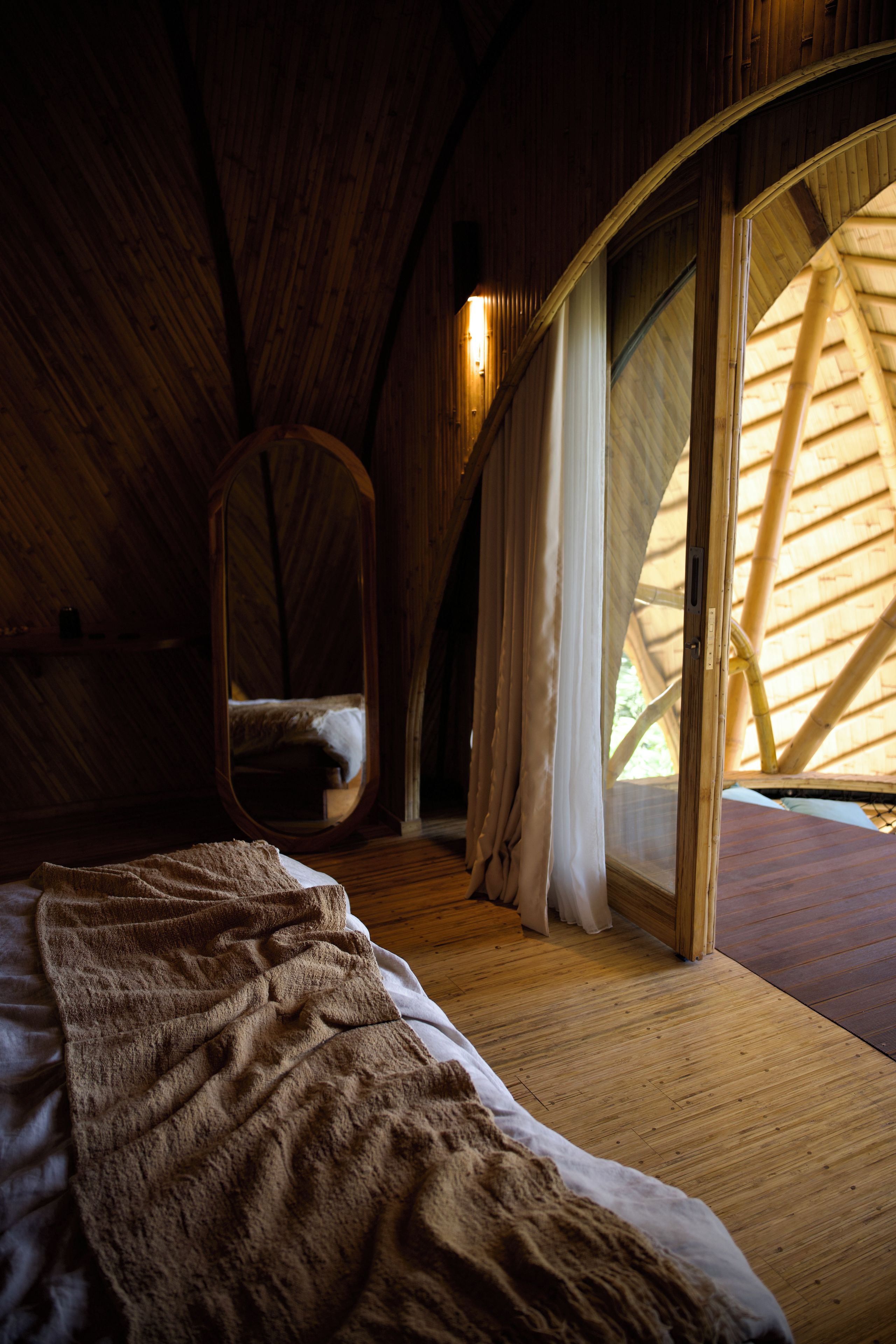 A cozy bedroom with a curved ceiling, a large bed, a hanging chair, and a window with a bamboo structure.
