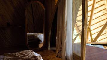 A cozy bedroom with a curved ceiling, a large bed, a hanging chair, and a window with a bamboo structure.