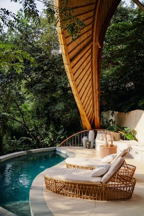 A poolside area with wicker furniture, a wooden structure, and lush greenery. - Cocoon Reserve (Kuta)