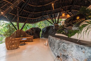 A thatched-roof outdoor seating area with a CocoN Reserve sign, surrounded by natural rock formations and greenery.