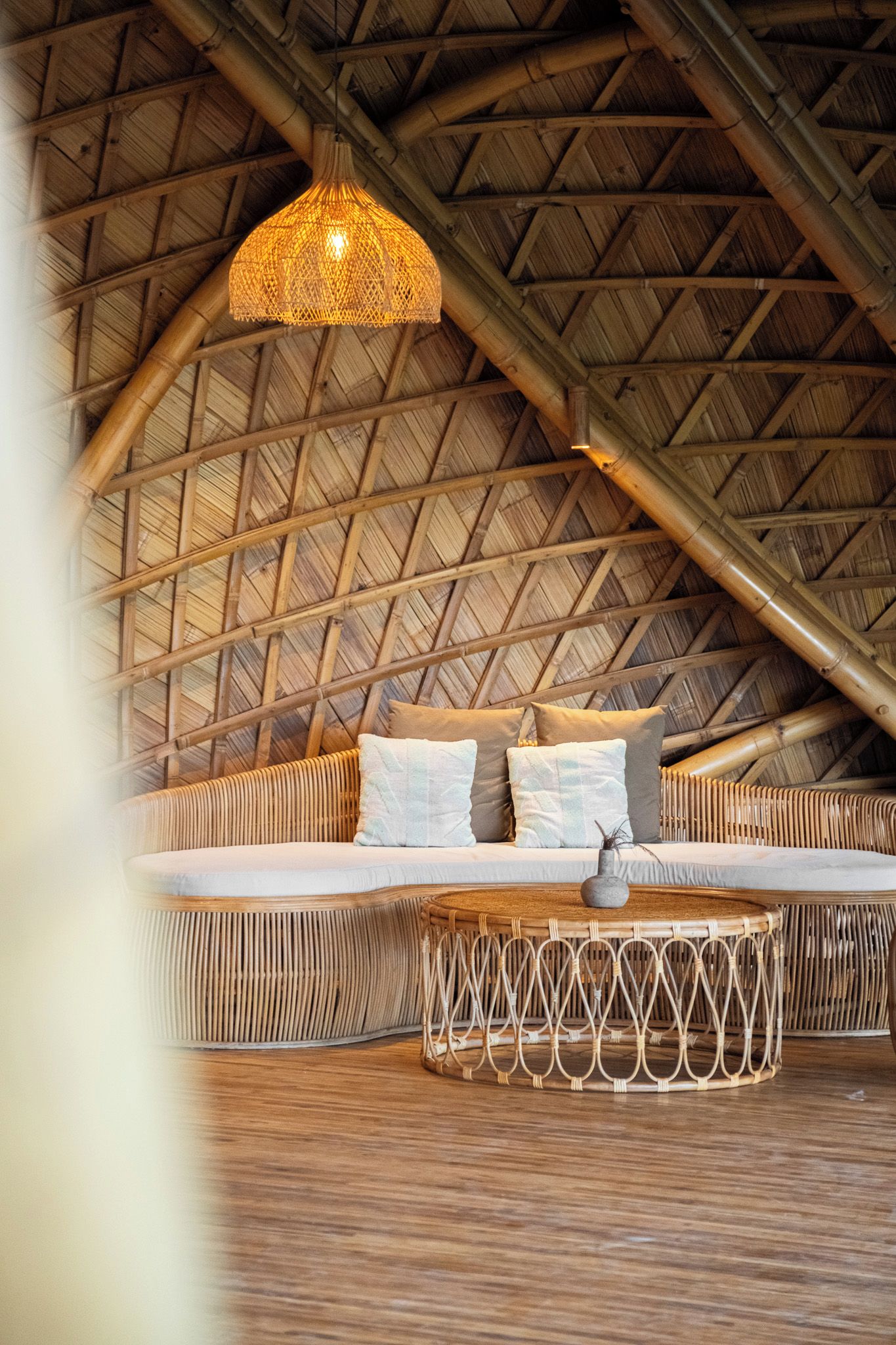 A room with a high ceiling, a woven ceiling, a bed with pillows, and a hanging light fixture.