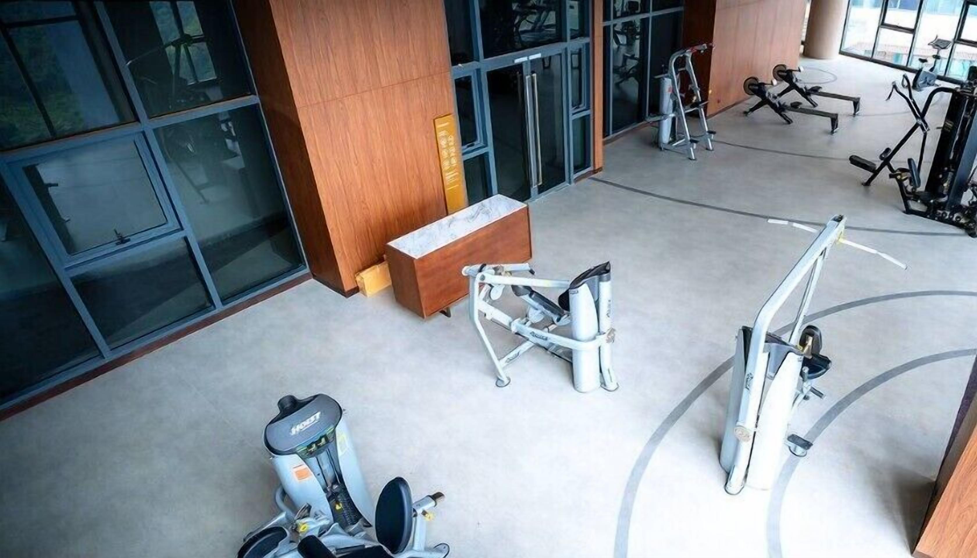 A gym with various exercise equipment, large windows, and a wooden bench.