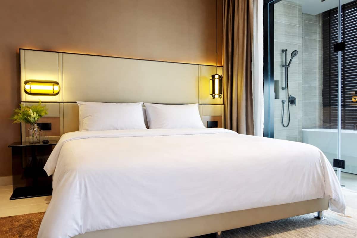 Une chambre d’hôtel avec un grand lit, des lampes de chevet, un vase de fleurs et une vue sur l’espace douche.