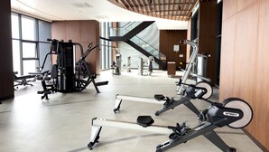 Ein modernes Fitnessstudio mit unterschiedlichen Trainingsgeräten, großen Fenstern und einer Holzbalkendecke.
