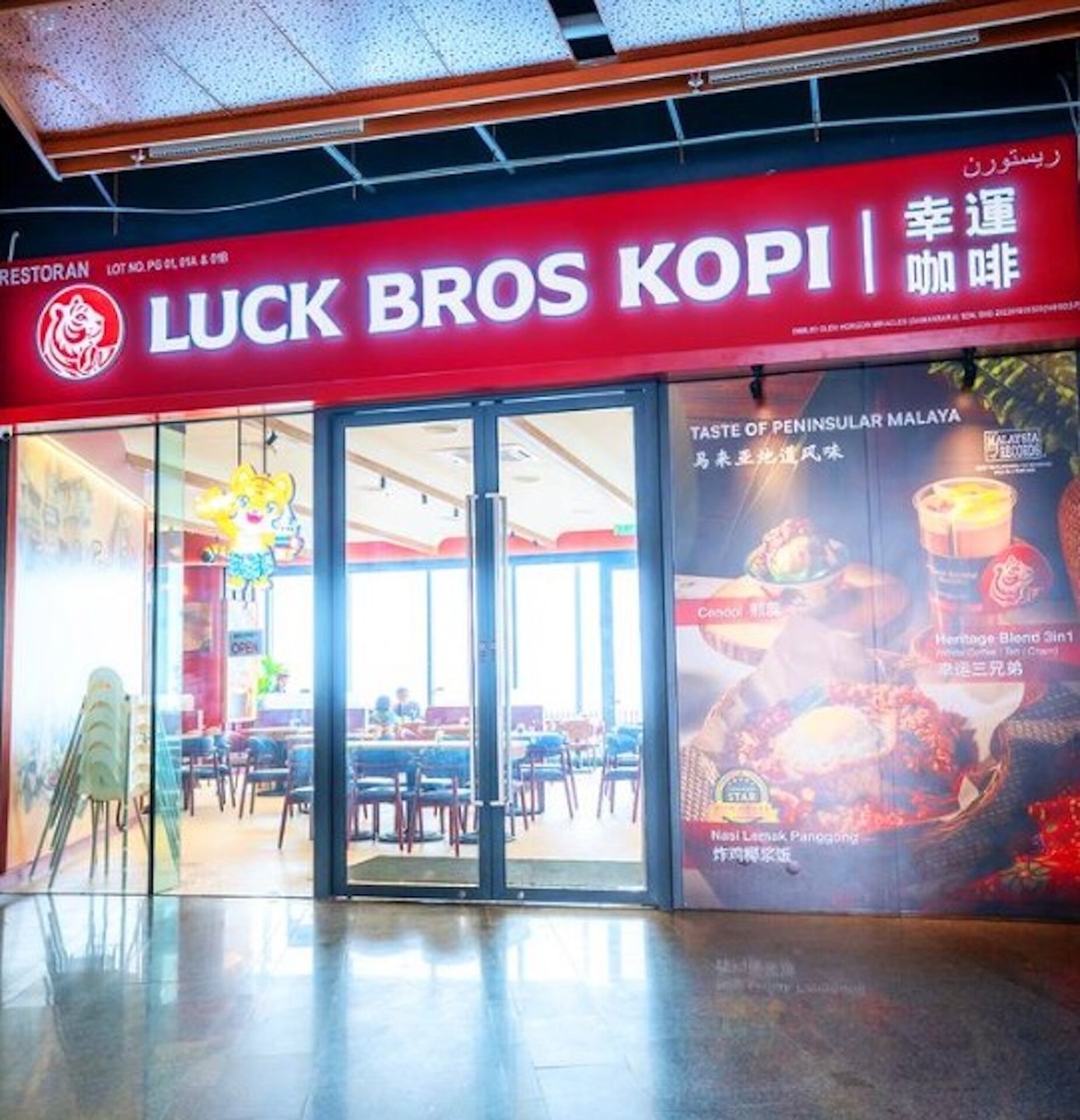 Ein Restaurant namens 'Luck Bros Kopi' mit einer roten Schrifttafel und Glastüren.