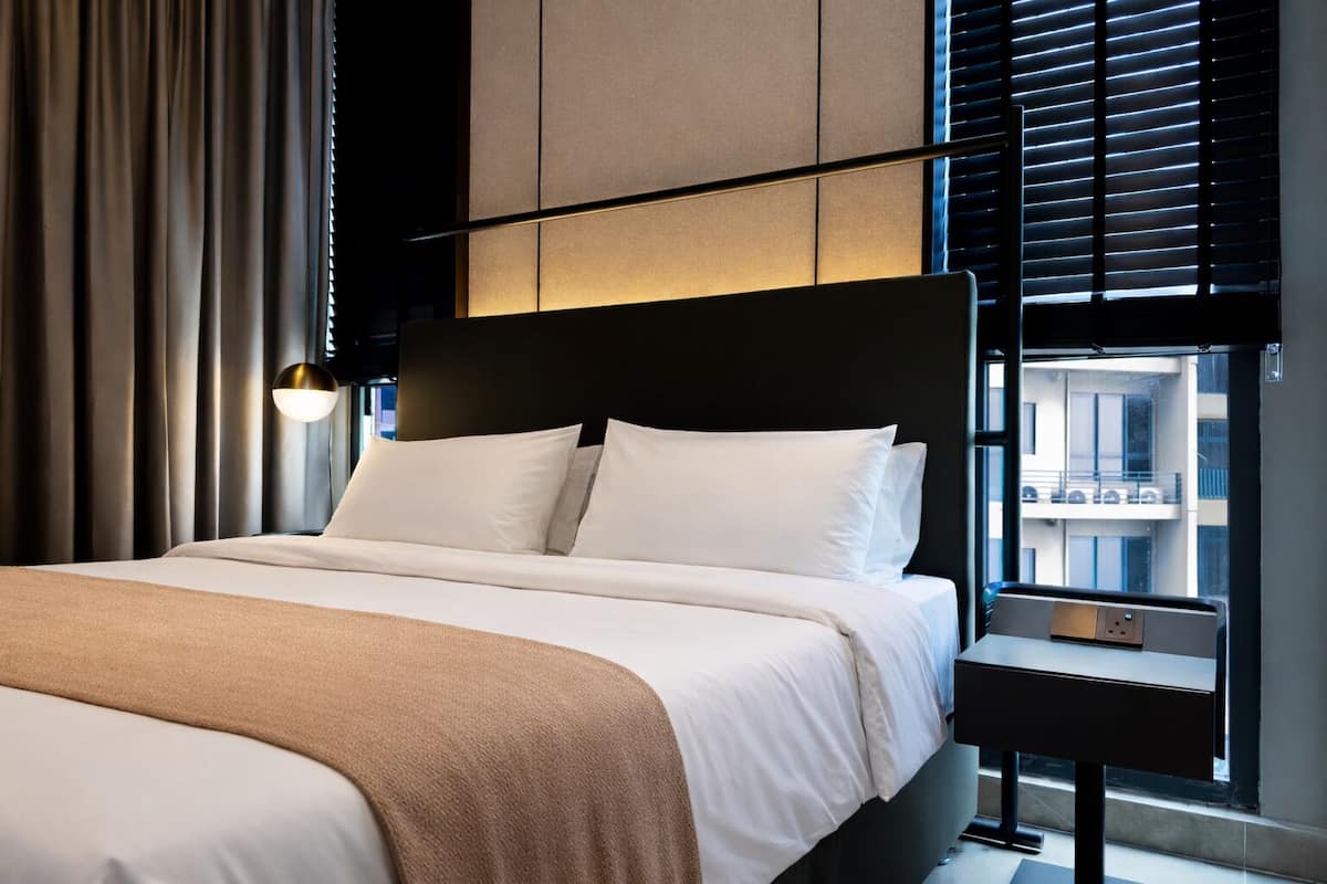 Une chambre d’hôtel moderne, dotée d’un grand lit, d’une table de chevet et d’une fenêtre avec des stores.