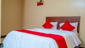 Un lit avec une literie blanche et des touches de rouge, une tête de lit en bois et un petit tableau accroché au mur.