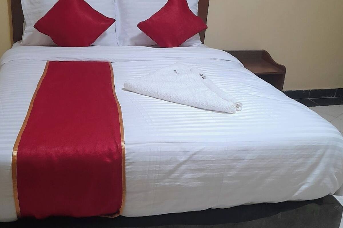 Un lit bien fait, avec une literie blanche et rouge, un couvre-lit rouge et doré, et une serviette blanche pliée posée sur le lit.
