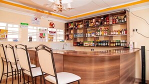 Un espace bar avec un comptoir en bois, de nombreuses étagères remplies de bouteilles d’alcool et des tabourets de bar.
