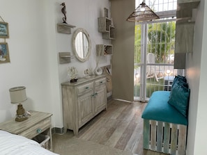 A bedroom with a bed, a dresser, a vanity, a mirror, and a window with a view of the outdoors.