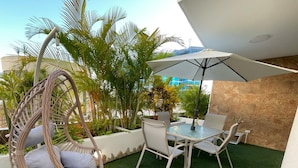 Un patio con una silla de mimbre, una mesa con sillas y una sombrilla.