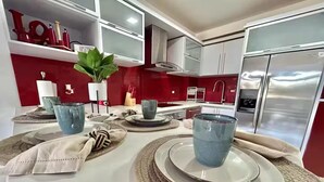 Una cocina moderna con encimeras blancas, salpicadero rojo y electrodomésticos de acero inoxidable.
