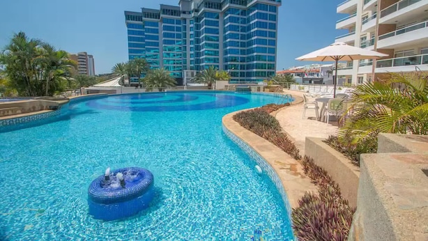 Una piscina con jacuzzi, rodeada de palmeras y edificios modernos.