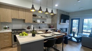 A modern kitchen with a central island, stainless steel appliances, and pendant lighting. - Bell`s Butte | Pool, Hot Tub & Fitness | Parking (Canmore)