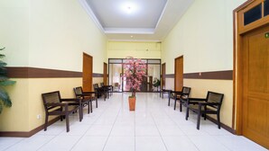 A hallway with wooden benches, a potted plant, and a door with a sign. - Guesthouse Pondok Tamsis by ARBA (Yogyakarta)