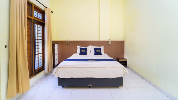 A hotel room with a bed, curtains, a nightstand, and a window with a view. - Guesthouse Pondok Tamsis by ARBA (Yogyakarta)