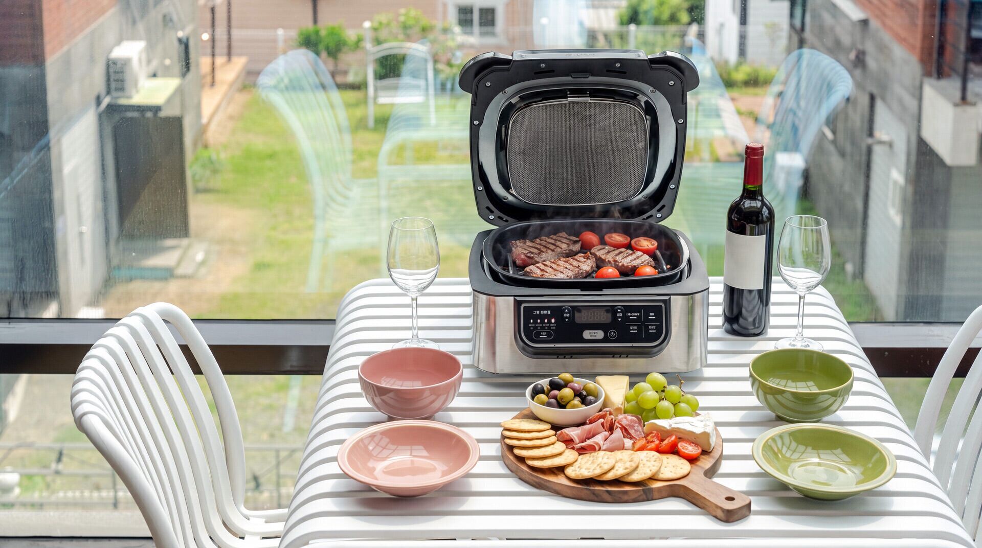 Varanda com mesa posta para refeição, incluindo churrasqueira, vinho e petiscos.