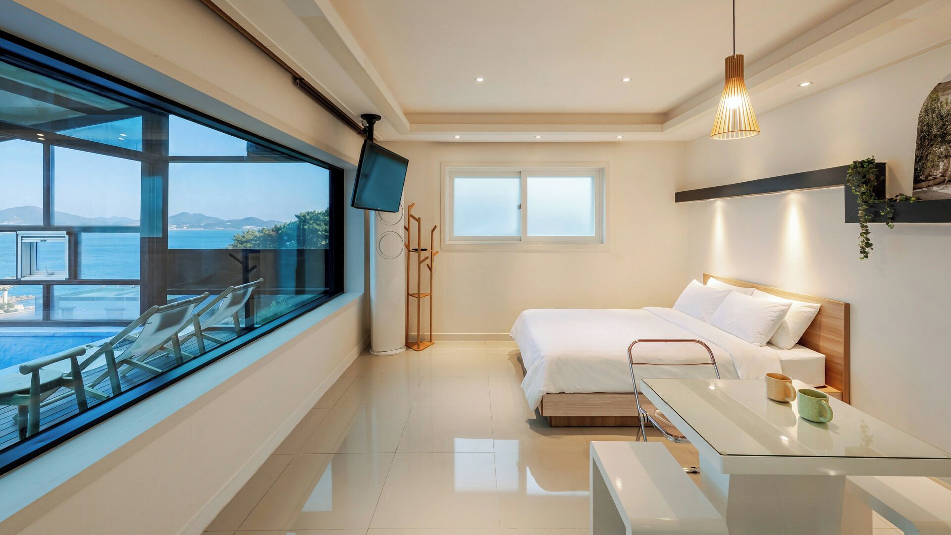A modern bedroom with a bed, bedside table, and a view of the sea.