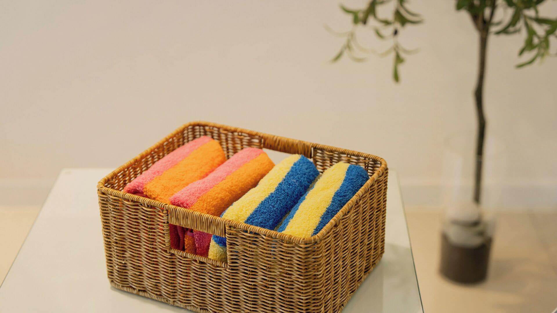 A wicker basket with colorful towels on a white table.