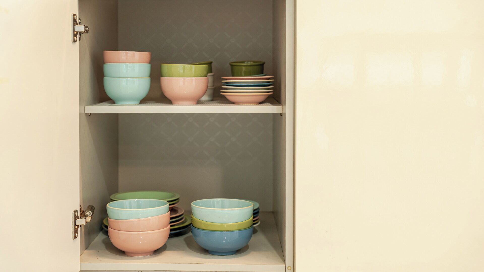 A cabinet with shelves holding stacks of bowls in various colors.