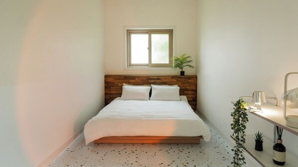 Une chambre à coucher avec une tête de lit en bois, une fenêtre, une table de chevet avec une lampe et une plante en pot.