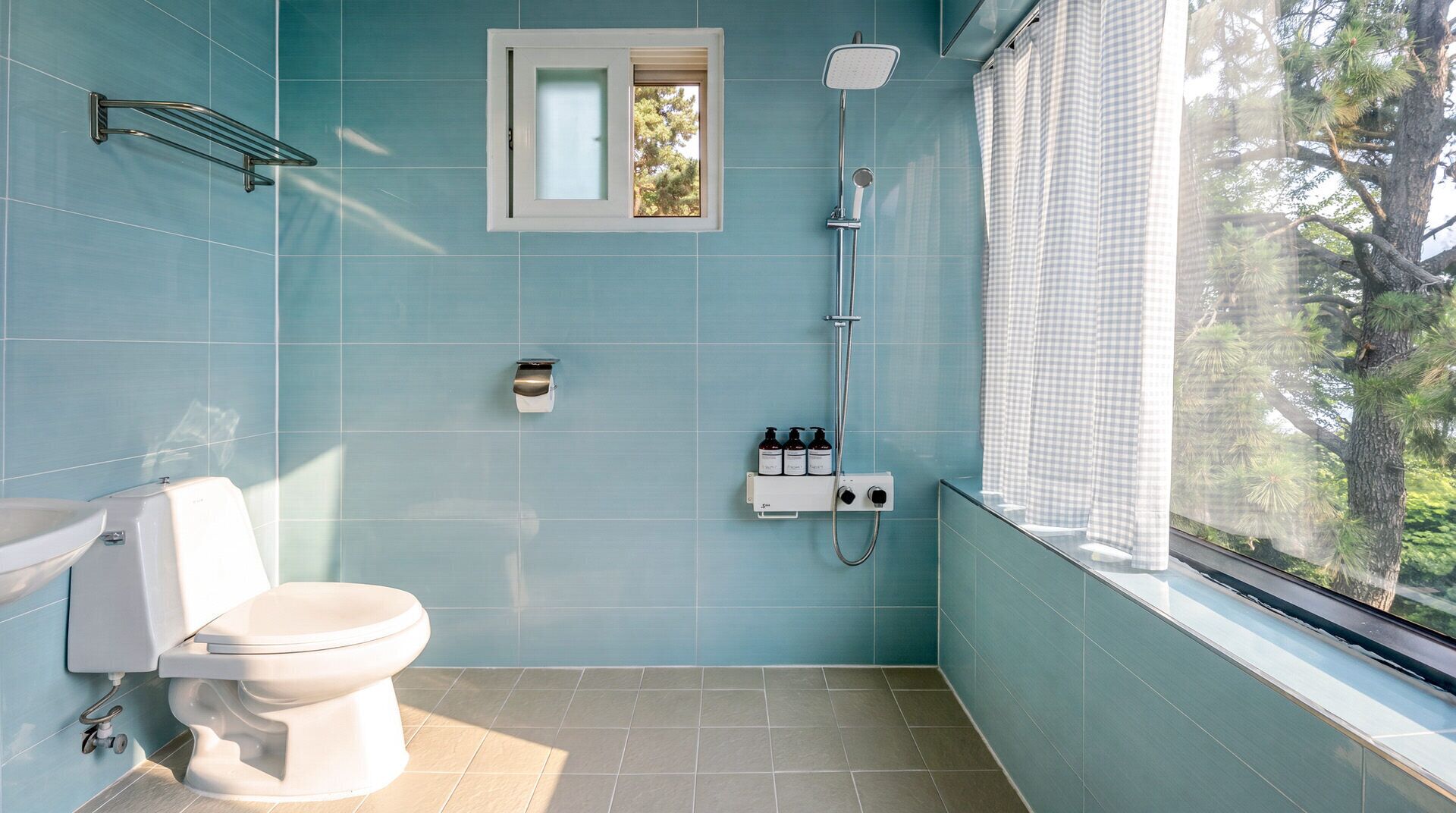A bathroom with a toilet, a shower, and a window with a view of trees.