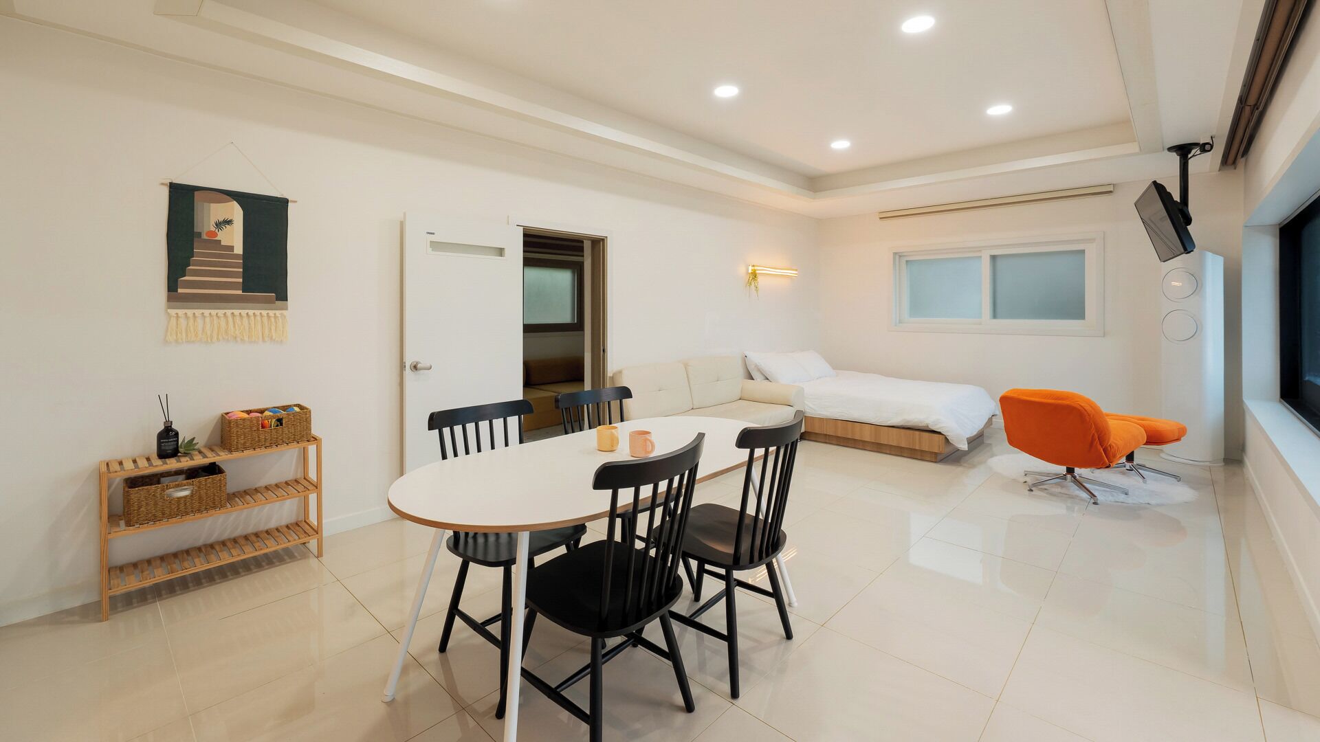 A modern room with a dining table, chairs, a bed, a sofa, a TV, and a window.