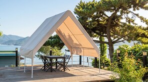 A wooden deck with a table and chairs under a tent-like structure, overlooking a body of water and mountains. - Geoje Stay Nangman (Geoje)