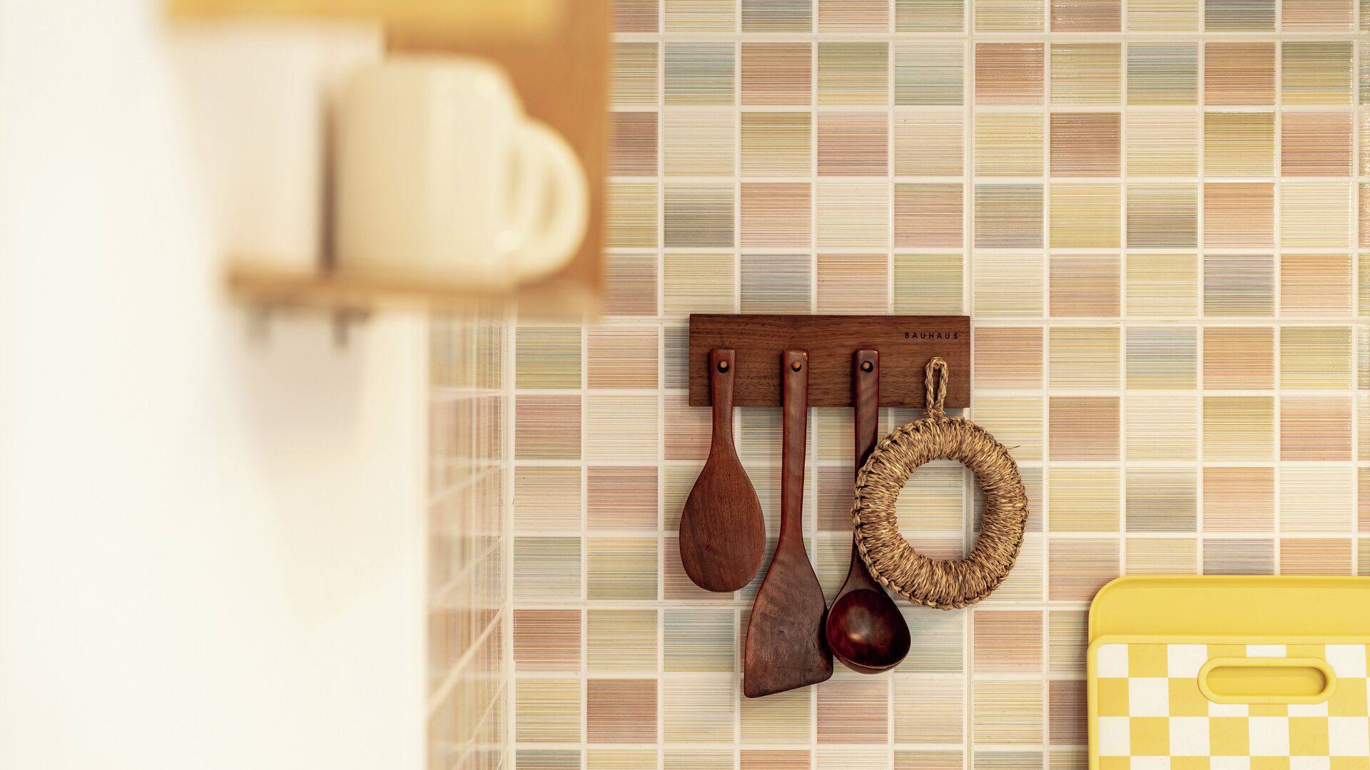 Una cocina con un escurridor de cucharas de madera, un anillo tejido y un artículo a cuadros amarillo.