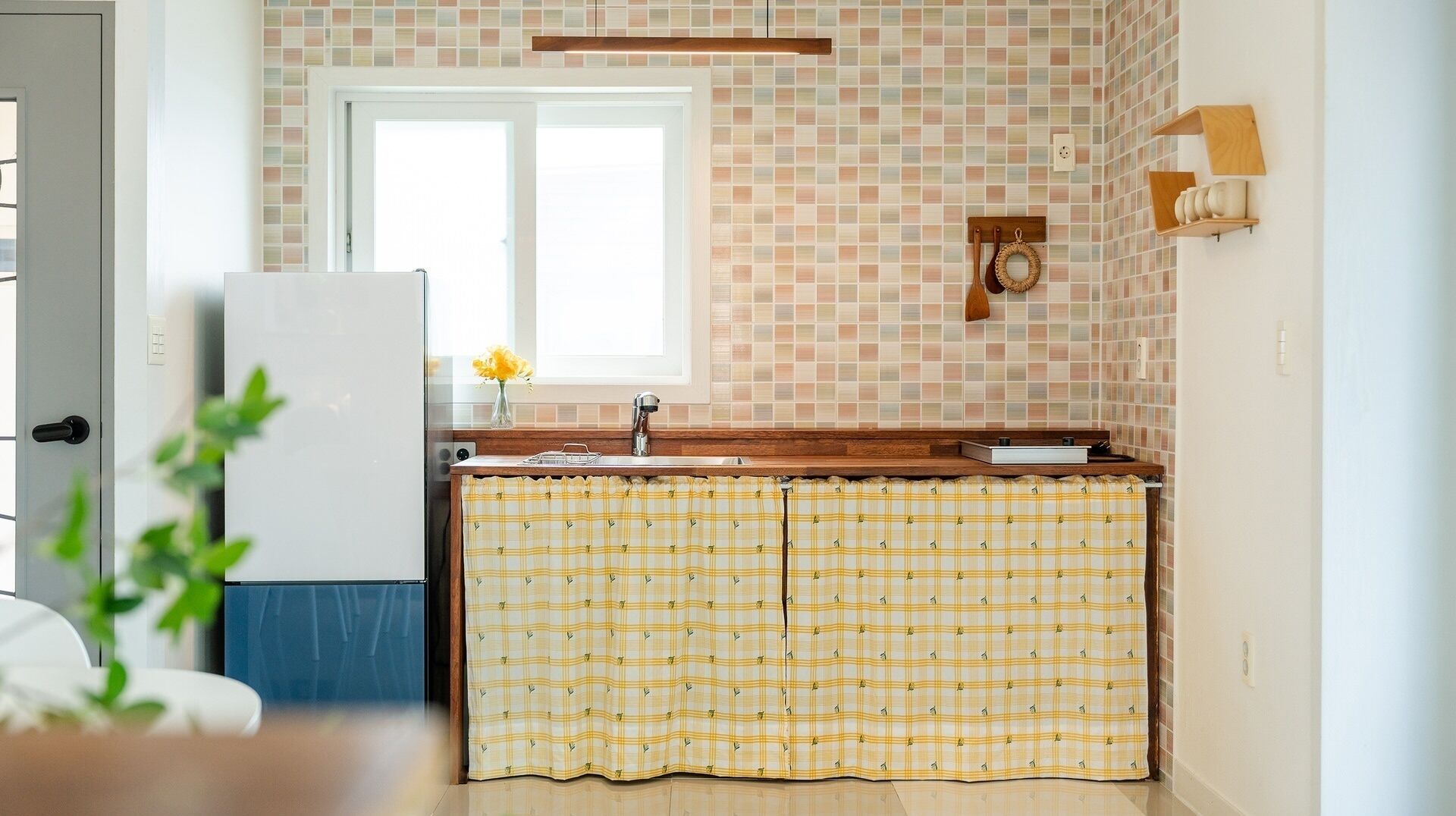 A kitchen with a window, a refrigerator, a sink, and a patterned curtain.