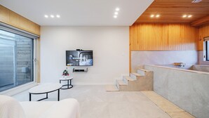 A modern interior with a flat-screen TV mounted on the wall, a small round table, and a staircase leading to a kitchen area. - Gyeongju Sanmaru Pension (Gyeongju)