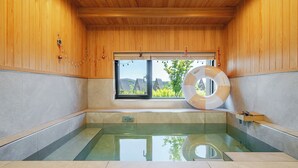 A wooden cabin with a glass-enclosed hot tub, a window with a view of greenery, and a life ring on the tub's edge. - Gyeongju Sanmaru Pension (Gyeongju)
