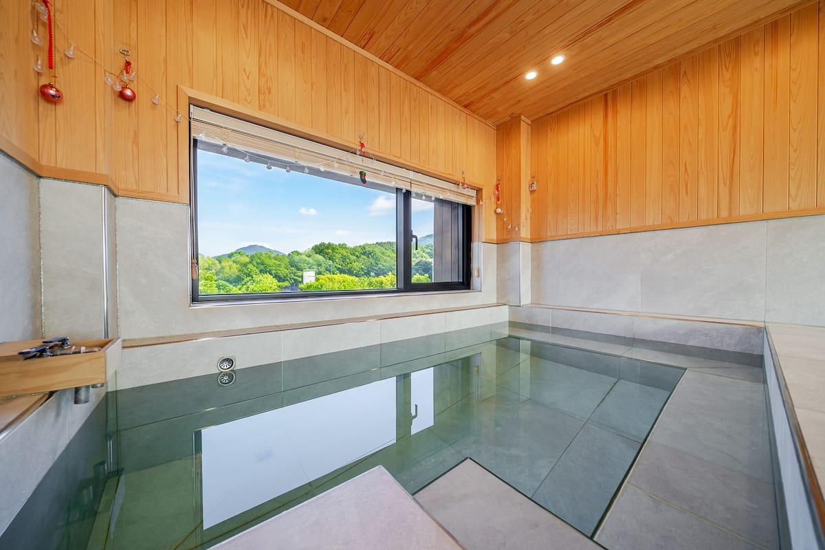 Une piscine intérieure moderne avec un plafond en bois et de grandes fenêtres donnant sur un paysage verdoyant.