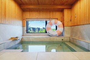 A wooden cabin with a glass-enclosed hot tub, a window with a view of greenhouses, and a lifebuoy hanging on the wall. - Gyeongju Sanmaru Pension (Gyeongju)