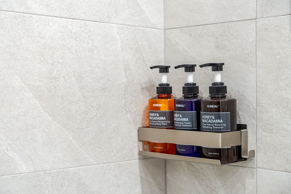 Een badkamerplank met drie flessen KUNDAL Honey & Macadamia body wash en shampoo.