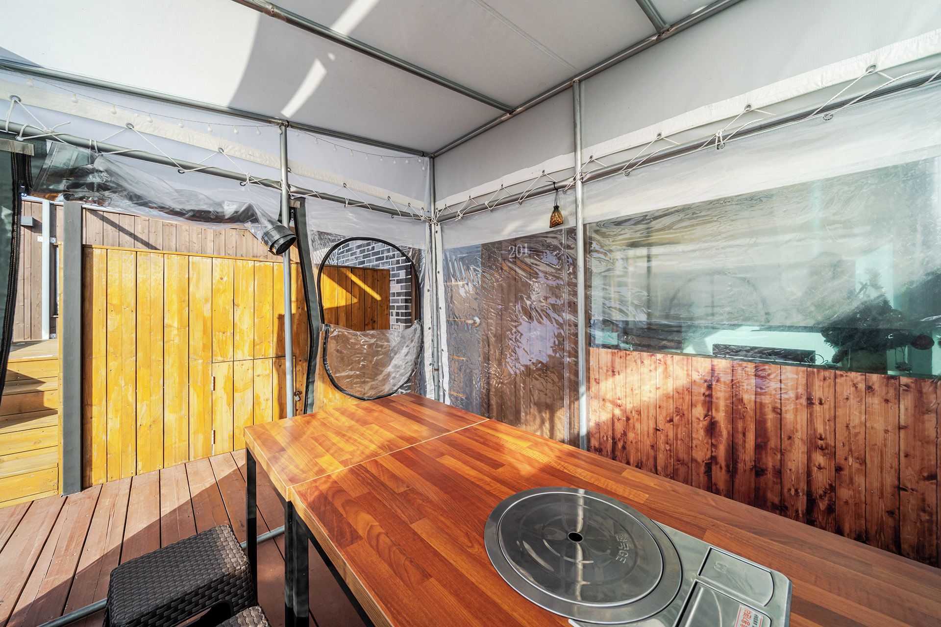 Una mesa de madera con tapa metálica, un banco de madera y vistas a un muro de ladrillo y una ventana.