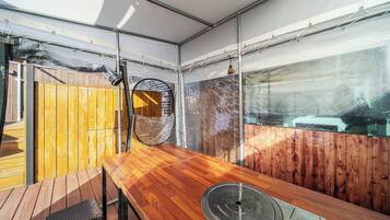 Una mesa de madera con tapa metálica, un banco de madera y vistas a un muro de ladrillo y una ventana.