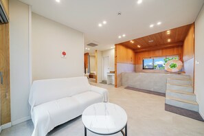 A modern interior with a white sofa, a round table, a wooden staircase, and a view of the outdoors through a window. - Gyeongju Sanmaru Pension (Gyeongju)